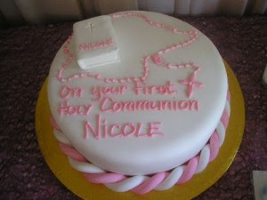 White cake with pink frosting reading "on your first holy communion Nicole"