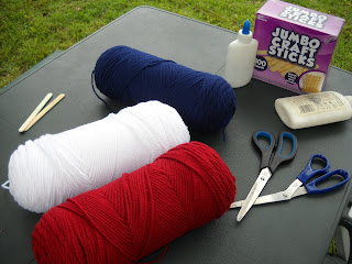 Blue, white, and red yarn with scissors, wood sticks, and craft glue