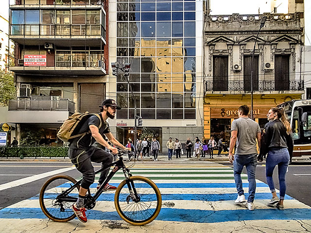 Ciclista y gente cruzando la línea peatonal(cebra)pintada de diversos colores.