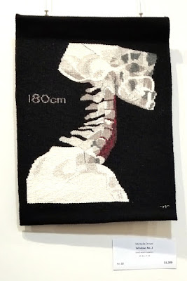 This monochrome woven tapesty depicts an X-ray of a person's shoulders, neck and the base of the skull and jaw, taken from the side.