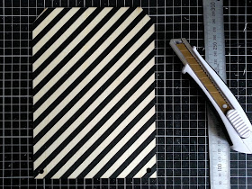 Rectangular piece of plywood bunting, printed with black stripes, laid out on a cutting mat along with a metal ruler and a utility knife.