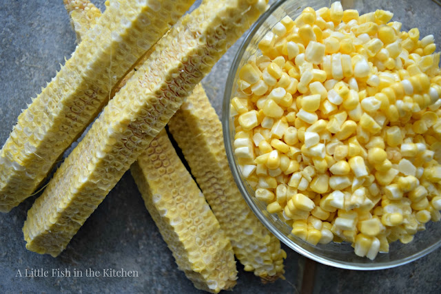 For raw corn husks rest near a clear glass bowl filled with their fresh corn kernels. 