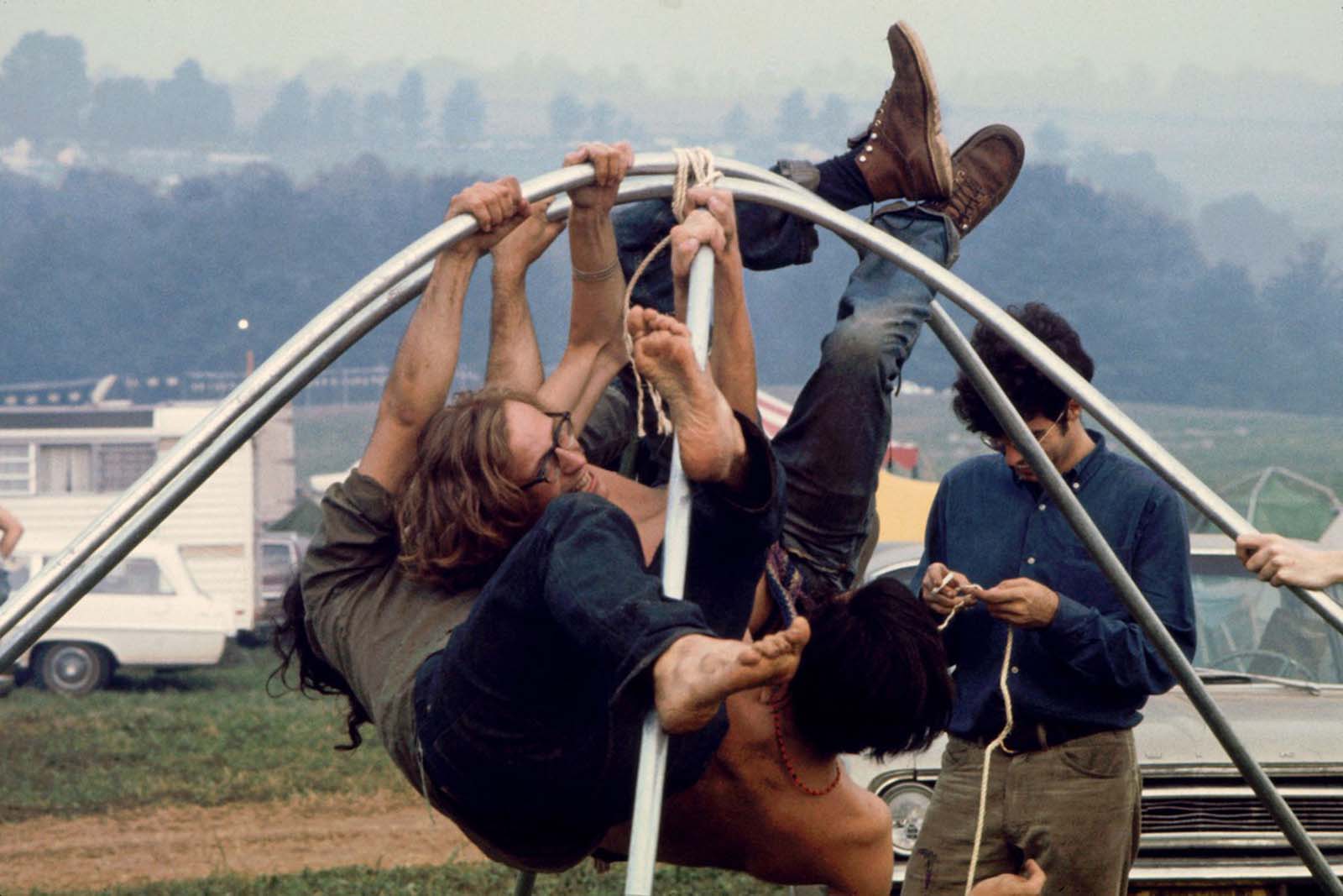 Festivalgoers hang from bent metal tubing as another untangles rope to tie the tubes together to form a tent frame on the grounds of the Woodstock Festival in August 1969.
