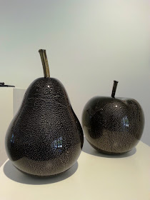 Large black and gold pear and apple on display in a gallery.