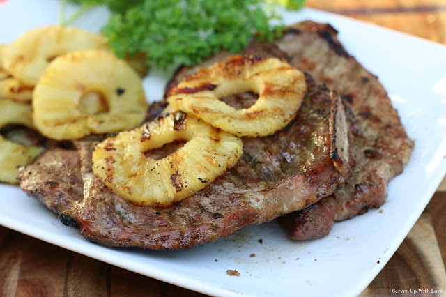 2 grilled pork chops on a white platter with grilled pineapple slices