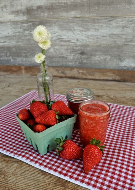 fresh strawberries next to strawberry jam in mason jar
