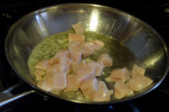The raw chicken being added to the skillet on the stove with the oil and butter to cook. 