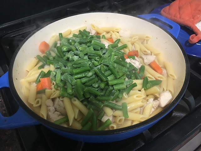 The frozen green beans in the pan with the cooked pasta, chicken and carrots.  