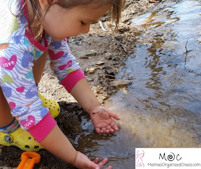 Young girl in pink shirt and yellow crocs putting her hands in a river to play
