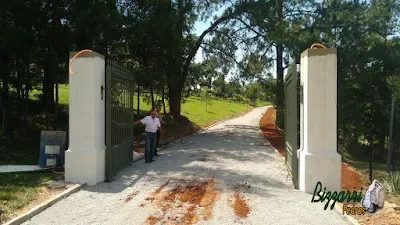 Execução das guias de pedra para executar a rua de pedra com pedrisco em entrada da fazenda em Atibaia-SP com os pilares do portão e o portão de ferro. Na foto, Bizzarri examinando os detalhes e no paisagismo o gramado com grama batatais.