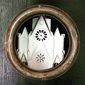 Detail of an assemblage art piece by Alex Asch, showing a cathedral model inside a circular port hole.