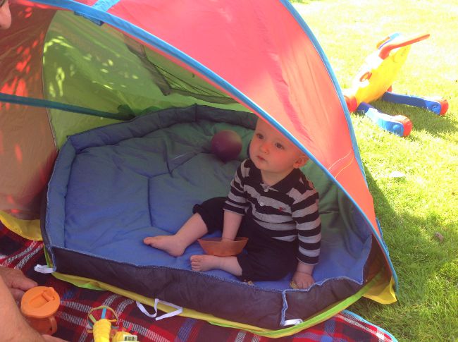 baby sat in tent in garden with blue padded base from playpen