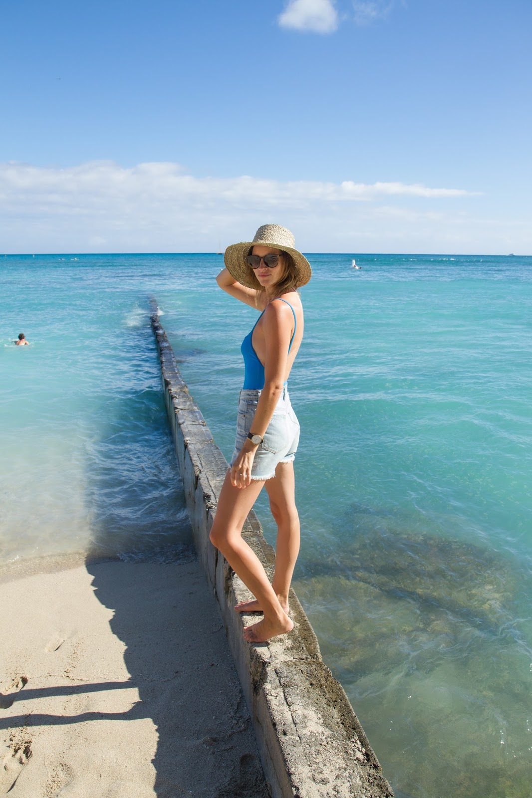 Fashion and travel blogger, Alison Hutchinson, is wearing a Solid and Striped swimsuit, Ksubi shorts, Saint Laurent Sunglasses and a wicker hat from Bali