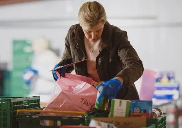 The Countess of Wessex visited the warehouse facility of the Woking Foodbank at Sheerwater. brown coat and pink sweater