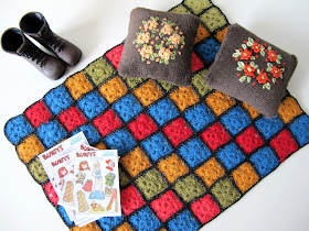 One-twelfth scale miniature 1940s afghan rug, embroidered cushions, tramping boots and paper dolls.