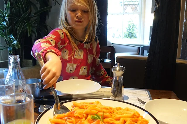 A young girl helping herself to pasta from a big bowl in the middle of the table at Prezzo