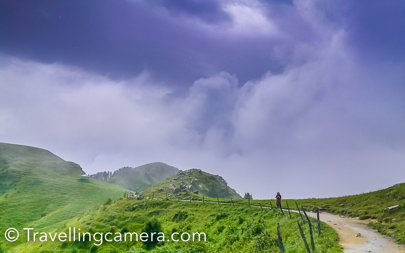 During my recent visit to Dalhousie, we planned to do a small trek to Dainkund (Temple Pohlani). This Photo Journey shares about our experience through clouds and how we beaten the rain. And if you are in Dalhousie during Monsoon, this trek is highly recommended. You literally walks through clouds and it's an easy trek.We drove through Kala Top to the base of this trek, which is entry gate of Air force base. We parked our car there and started the trek. There is well paved path for 1 km, which is maintained by temple authority. This path certainly made our lives easy during monsoons.This is a view after walking up for 250 meters. This road goes down to Dalhousie and Kala Top.As we started the trek, rain started and we thought of skipping it and going to Khajjiar instead. But in few minutes we encouraged each other to use umbrellas and start climbing up. And at the end it proved to be rewarding.Clouds were playing hide and seek with us. At times, they were chasing us and in few minutes sun was shining by clearing them away.Throughout the trek you are exposed to some breathtaking views of valley full of high deodars and birds flying all around. We saw few colorful butterflies on our way but couldn't click them well.We did the trek at our own pace. Stopped many times and enjoyed quick snacks which we were carrying with us. And Urvi was always ready to pose :)On the way, there is a temple which is 2.5 kilometers away from road. Lot of local folks visit this temple. Interesting most of the temples in this region don't have roofs. There is a little shop near the temple from where you can buy snacks and juices.While walking through the mountains, Vibha pointed towards this cloud form. With a smile she says - 'doesn't it look like a giraffe?'. Do you think so?There is a beautiful view through clouds. Most of the times clouds stopped our view of surroundings but such views through clouds were very special.This is 3 kilometers trek which means you need to walk for 6 kilometers. And we had 3 years old trekker with us. Mentioning that to share that anyone can do this trek. It's very easy and the experience can be very rewarding. On a clear day, Khajjiar is visible from top.Panoramic views from top were mesmerizing.There is small shelter on the way. We took a break here where it started raining heavily.Every now and then we were stopping to views awesome scenes all around us. Here Urvi is trying to locate Khajjiar :)Not sure what Indu is trying to do on phone because there is no signal on these hills :) . Probably checking the photograph she just clicked with her phone.We reached there quite early and met this gentleman. He offers horse riding to tourists coming to this place.Urvi loved walking throughout and showing some interesting views to us. Vibha and Urvi were most observant from the lot.It was time to head back and don't miss to watch time-lapse videos shared below.