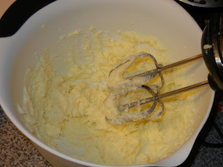 butter and sugar being creamed in a white bowl with a hand mixer 
