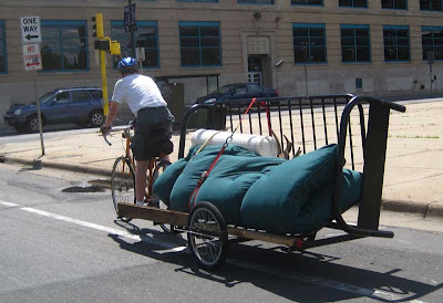 Bicyclist pulling a trailer with a futon sofa frame and futon attached