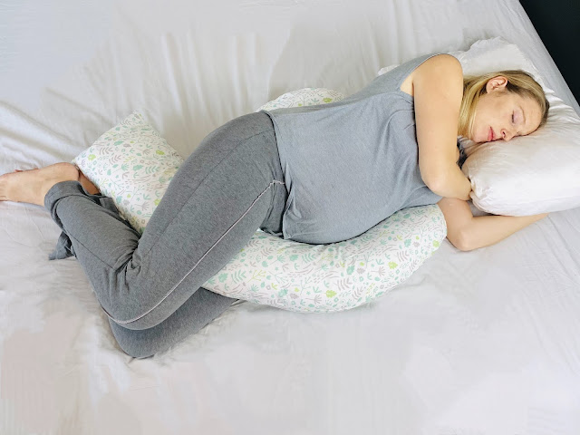 Me in grey PJs lying in a sleeping position with the dreamgenii pregnancy pillow