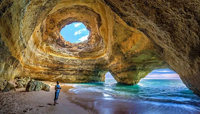 stunning cave with deep bluw water and man on sand looking up
