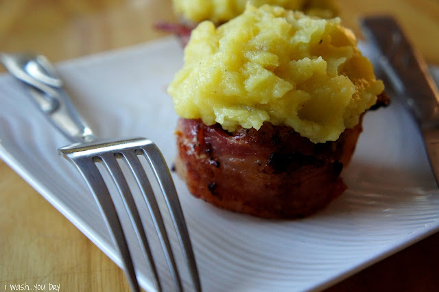 A close up of bacon wrapped meatloaf topped with mashed potatoes displayed on a plate.