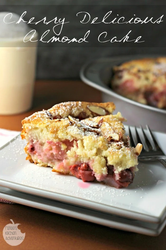 Cherry Delicious Almond Cake slice on a white plate with the rest of the cake in the pan in the background