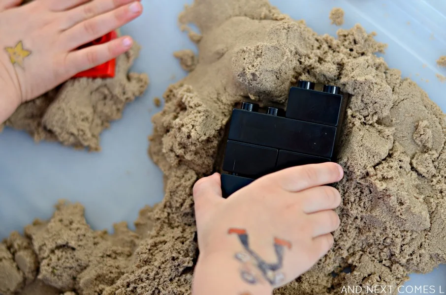 Pressing and stamping LEGO duplo into a kinetic sand sensory bin