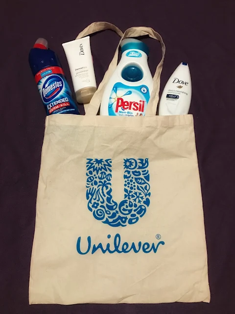 A fabric bag with a "U" on and the Unilever logo with a bottle of Domestos, Dove body lotion, persil non bio and Dove bath cream