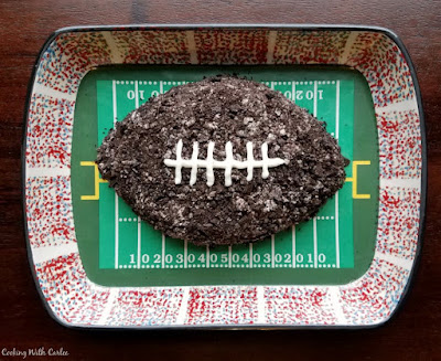 This sweet cookies and cream cheese ball is the perfect game day dessert. It is full of chocolate goodness and goes with a ton of fun dippers. Grab a bite and enjoy the big football game! cookies and cream cheese ball shaped like football on a football field platter
