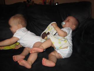 twin baby girls sitting on a couch and rolling away from the camera