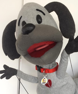 the light gray puppet of Scooter from Scooter & Boots, wearing a red collar 