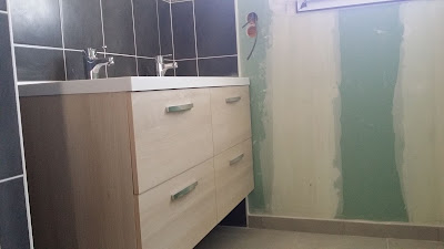 Salle de bain terminée avec la faïence murale, douche, lavabo double vasque sur meuble de salle de bain. Le carrelage est également terminé.