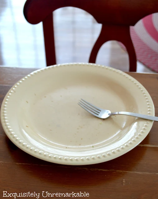 An empty yellow dinner plate and a fork on a wooden table