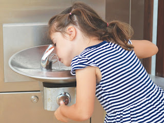 kleines Mädchen, das aus dem Wasserbrunnen trinkt 