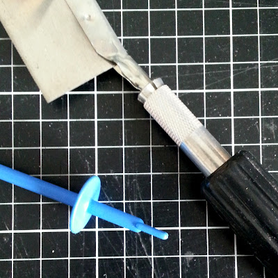 Aerial view of a cutting mat with a saw and a plastic length with a cirular protuberance near the bottom. 
