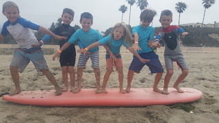 Six kids standing on a surfboard