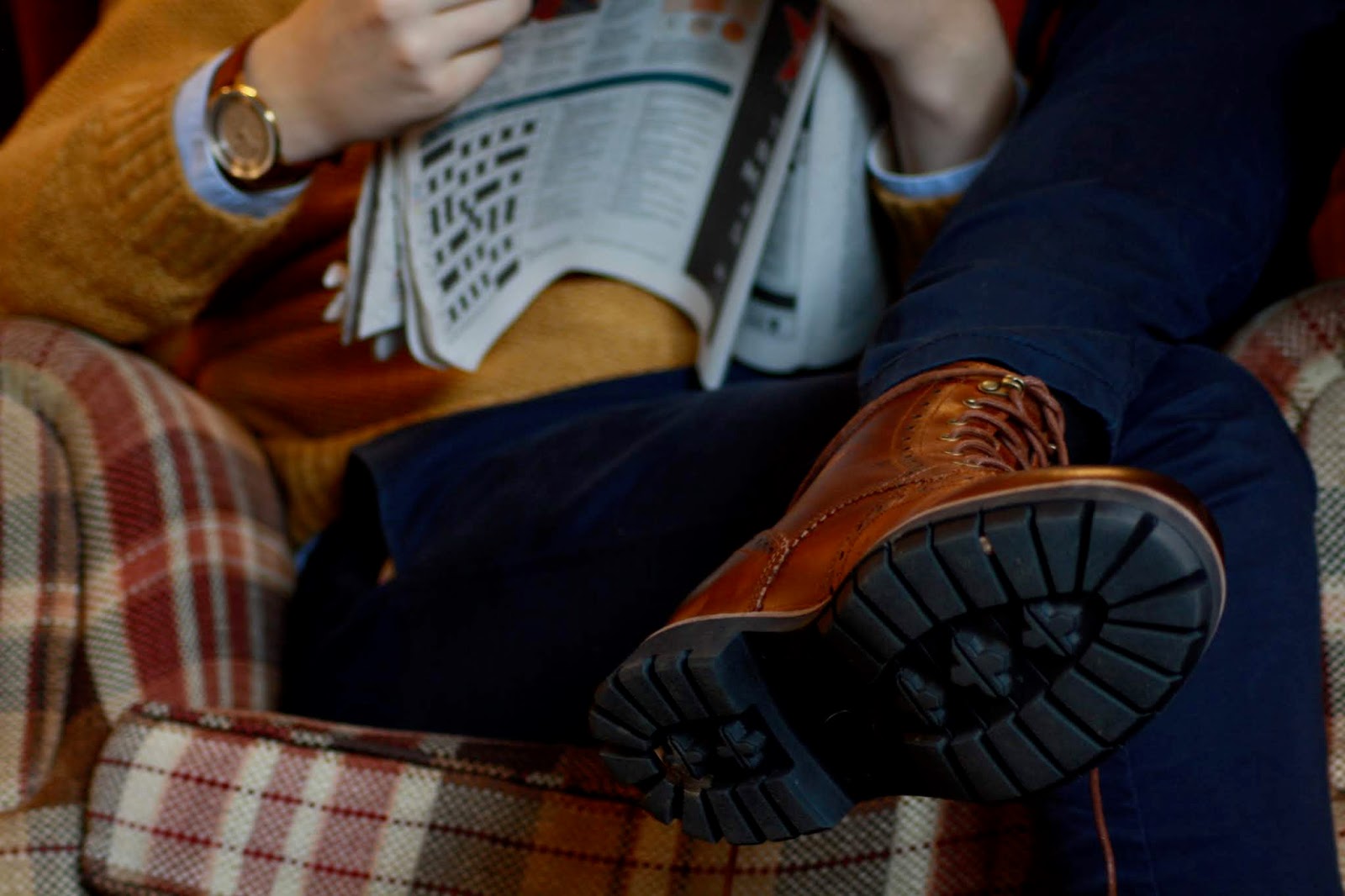 close up of a men's outfit comprising dark tan boots and watch, mustard jumper and blue trousers