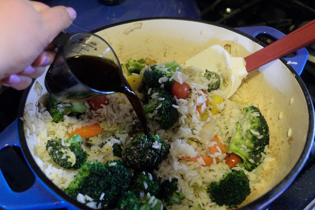 The teriyaki sauce being added to the pan with the vegetables and rice. 