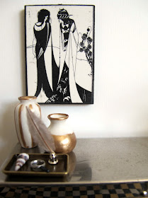 Art deco style modern miniature silver sideboard with a black and white picture hung above it and a selection of white and gold items displayed on it.
