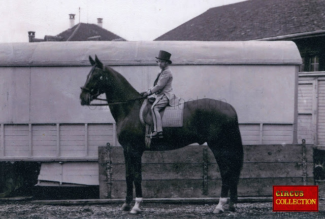 Photo de presse du cirque Knie en 1929 représentant Fredy Knie senior vêtu d'un smoking et d'un chapeau haute forme montant son cheval , avec une roulotte en arrière plan