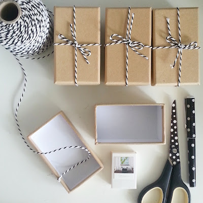 Three brown gift boxes tied with black and white twine next to a cone of twine and an open box. At the bottom left is a matchbox calendar, a pair of spotty scissors and a spotty pen.