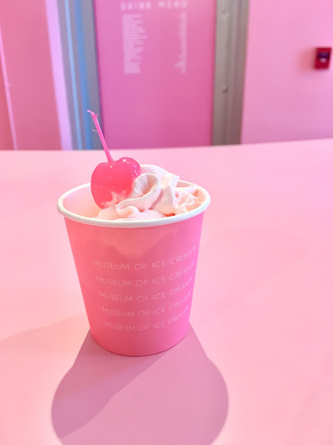 A small pink cup with pink whipped cream and a pink cherry on top