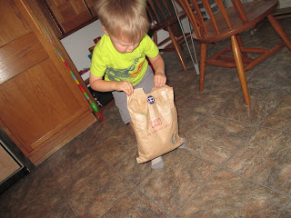 Toddler boy in yellow shirt trying to open brown paper package