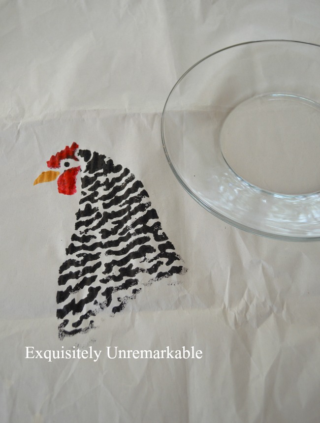 Painted chicken stencil on paper next to a glass plate