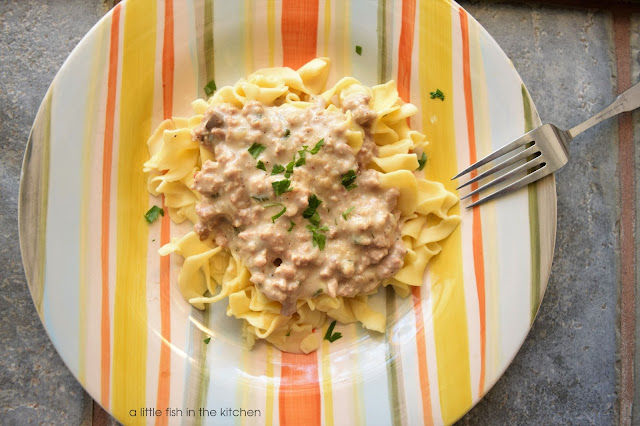 Creamy, comforting ground turkey stroganoff is served over tender cooked egg noodles. The single serving is on a colorful striped ceramic plate and a fork rests on the side.