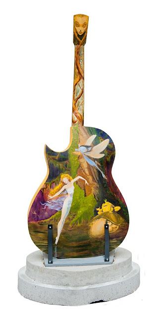 a large wooden guitar painted by a local artist with a scene from the woods with fairies, downtown Orillia