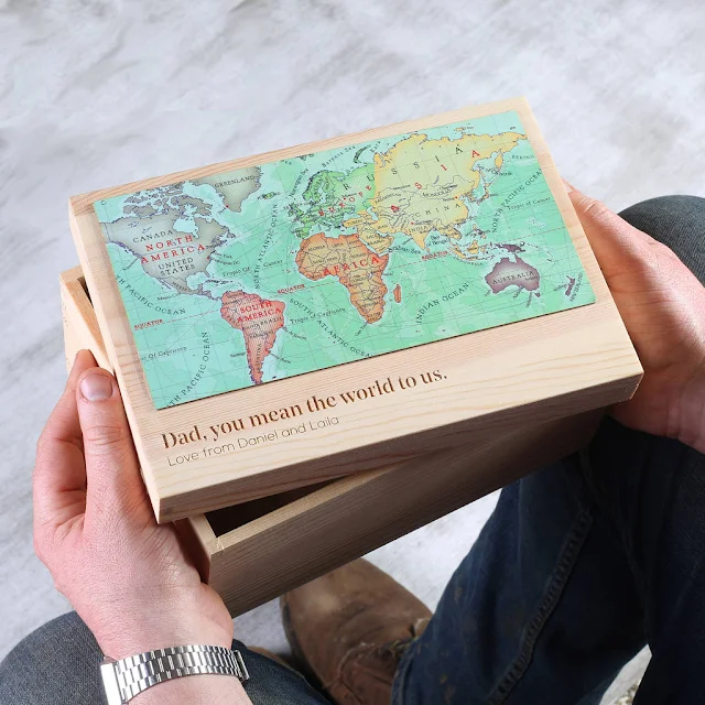 A pair of hands holding a small rectangular wooden box with a map of the world on it and a message engraved saying "Dad, you mean the world to us. Love from Daniel and Laila"