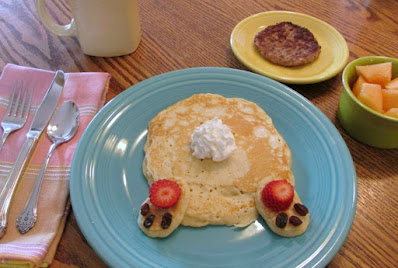These bunny butt pancakes are cute as can be and they come together so quickly. What a great way to treat your family on Easter morning! bunny butt pancake on blue plate with a small bowl of melon and sausage patty
