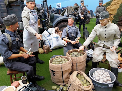Four 1/6 scale German soldiers peeling potatoes in diorama of an army post on display at a scale model exhibition.